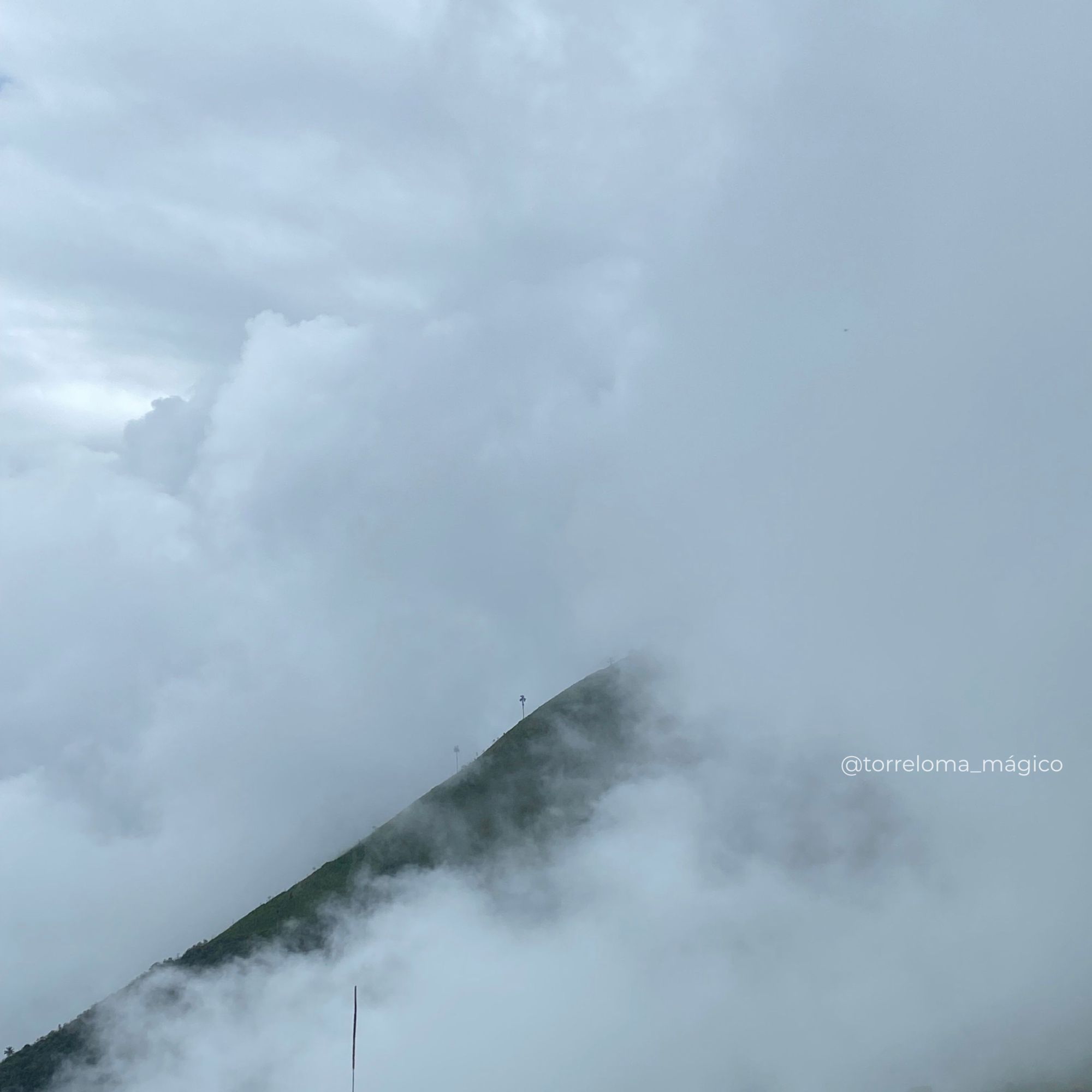 Una toma atmosférica que captura una cresta de montaña oscura y afilada emergiendo a través de un denso manto de nubes blancas en Torreloma. El cielo superior es gris plomizo y está cubierto de nubes de tormenta.
