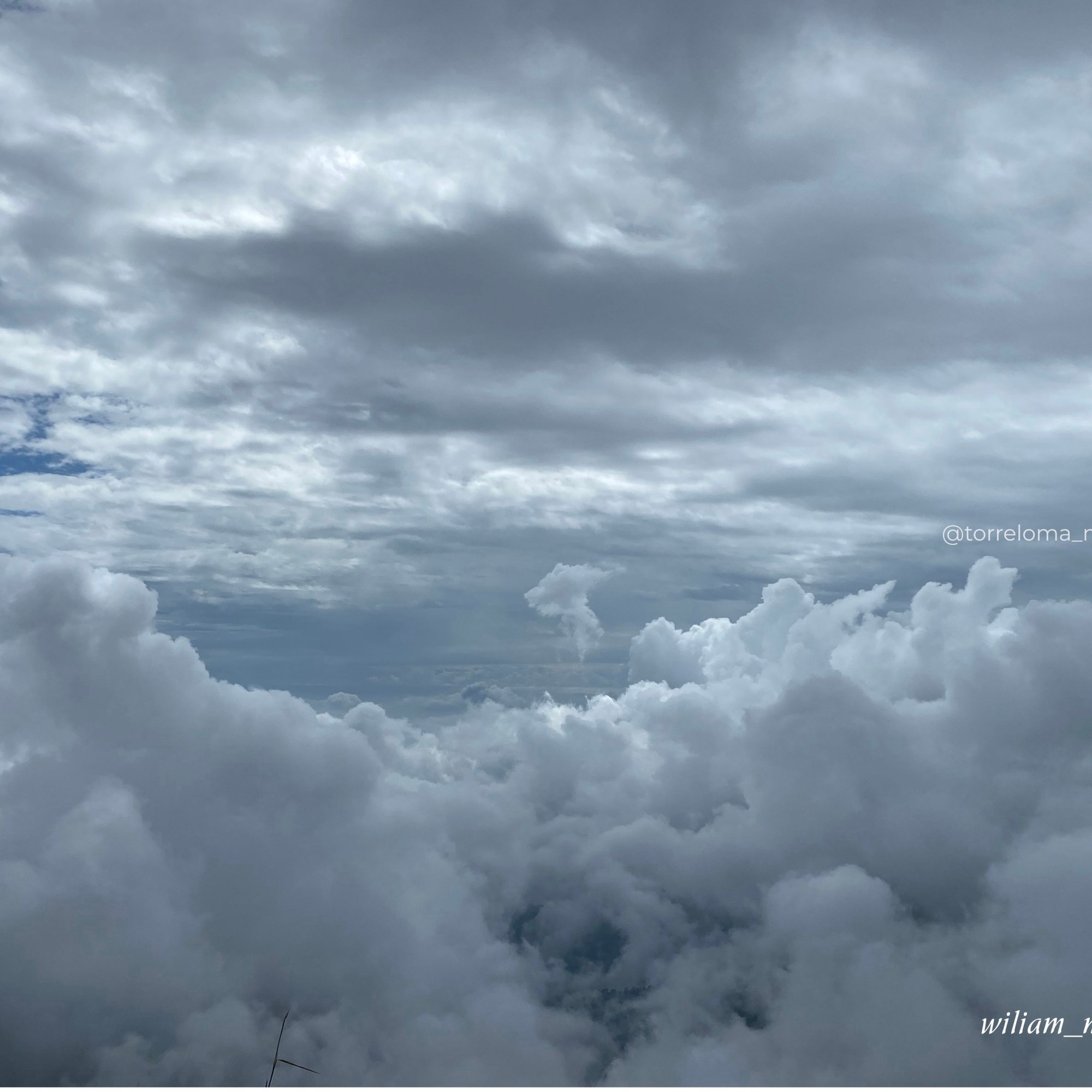 Una toma aérea de gran angular que muestra un vasto mar de nubes blancas y densas en la parte inferior, bajo un cielo nublado y estratificado de color azul profundo que llena la mayor parte del encuadre. La luz natural ilumina la parte superior del mar de nubes.